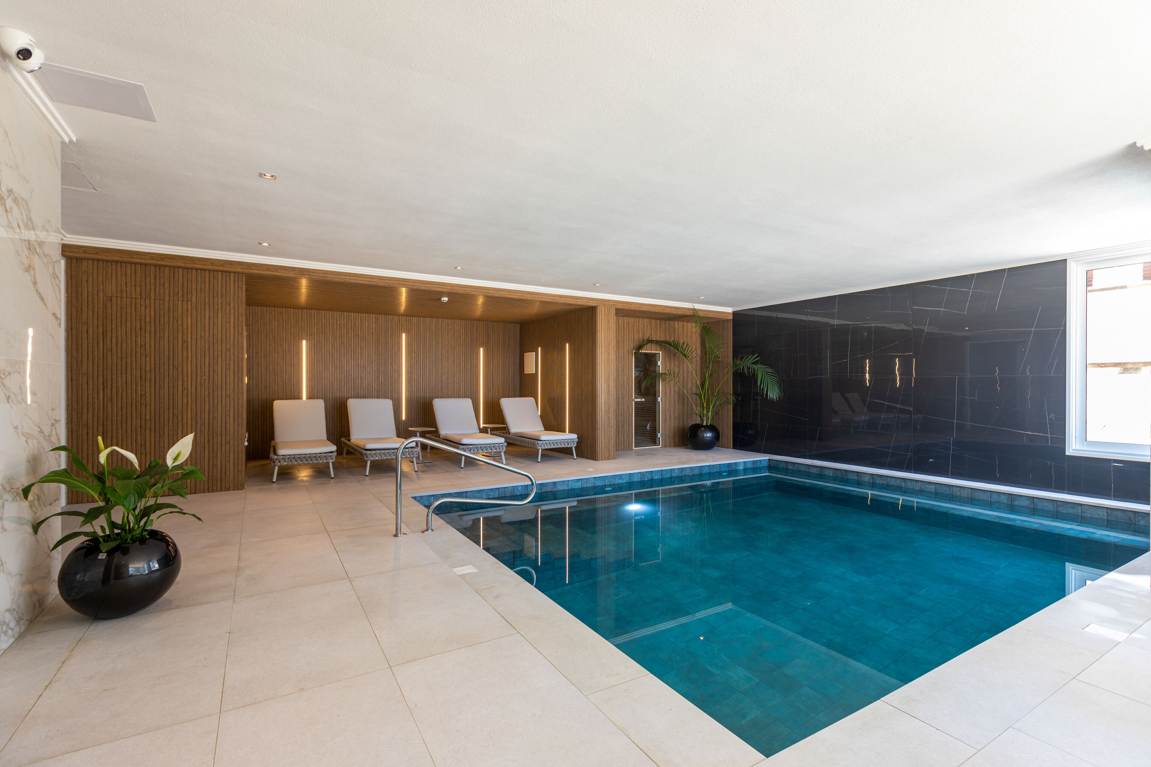 Una piscina interior moderna con sillones de descanso y una planta en maceta.