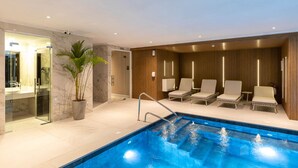 A modern indoor pool area with a glass-enclosed shower, lounge chairs, and a potted plant. - Hotel Solerios Mansa (Punta del Este)