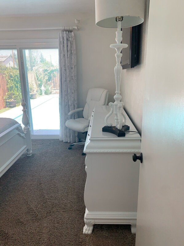 Una habitación de hotel con una cama blanca, un tocador blanco, una silla blanca y un ventanal con vistas al exterior.