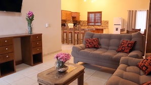A living room with a sofa, coffee table, and a desk. There is a kitchen in the background with a refrigerator and a dining area. - Hacienda Bella Cabo San Lucas (Apartment 2) (Cabo San Lucas)