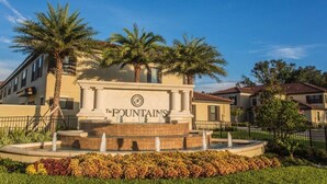 A fountain with a sign reading "The Fountains" surrounded by palm trees and a well-maintained lawn.