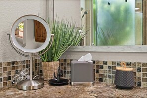 A bathroom vanity with a round mirror, a potted plant, a tissue box, and a soap dish.