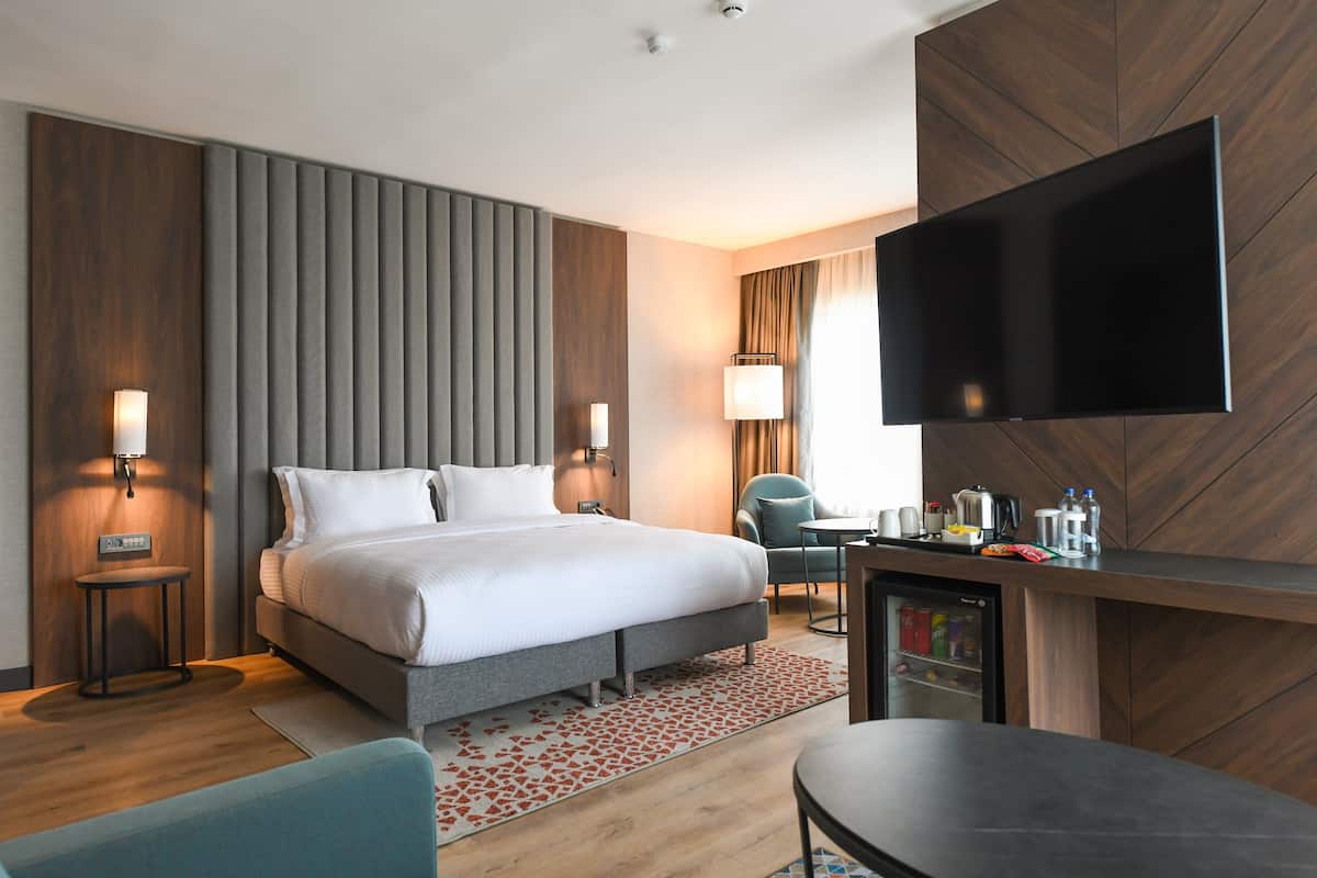 A modern hotel room with a bed, bedside tables, a TV, a desk, and a mini-fridge.