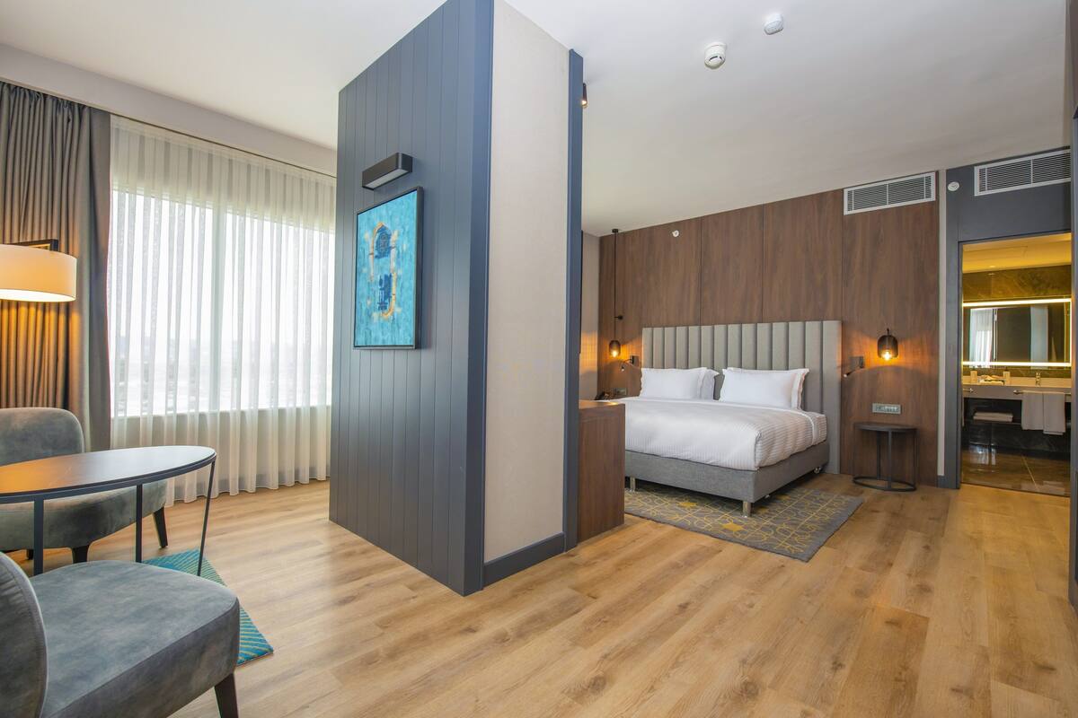 A hotel room with a bed, a desk, a chair, a lamp, and a bathroom.