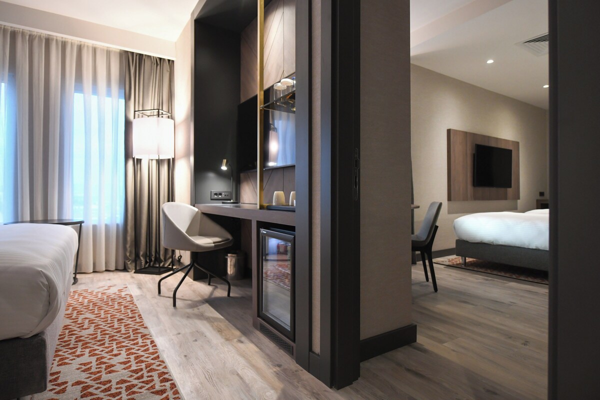 A modern hotel room with a bed, desk, chair, and a television mounted on the wall.