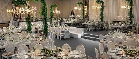 Une salle de banquet avec des tables rondes, des chaises blanches, des lustres et des décorations florales.