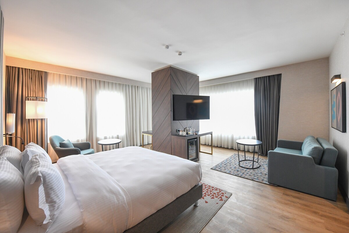 A modern hotel room with a large bed, a sofa, a TV, and a desk.