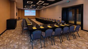 Un salón de conferencias con una larga mesa, sillas y una pantalla de proyector que muestra “CROWN PLAZA ANTING HOTEL ANKARA”.