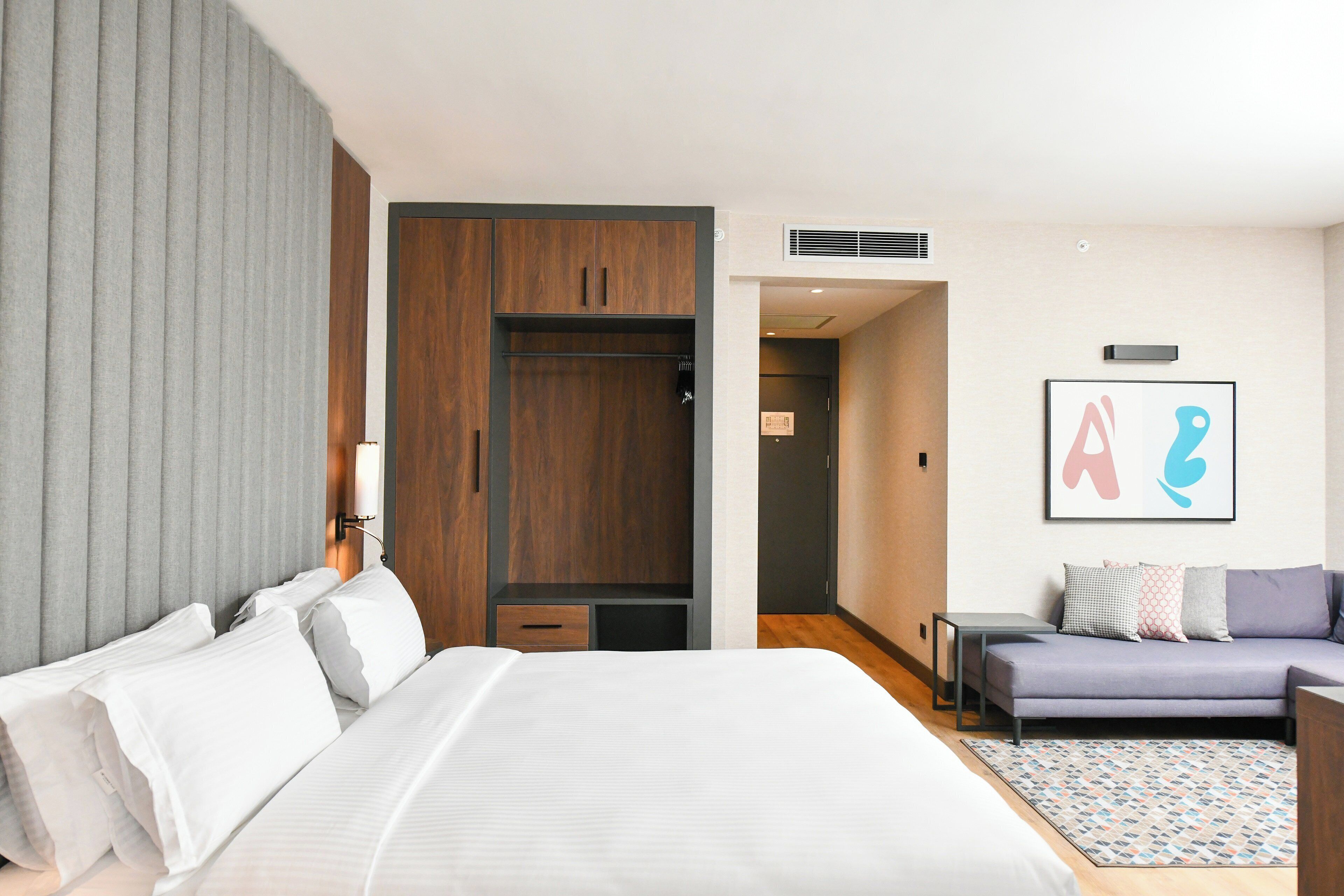 A hotel room with a large bed, a sofa, a wardrobe, and a bathroom visible through an open door.