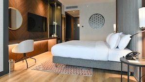 A modern hotel room with a large bed, a desk with a chair, a round mirror, a flat-screen TV, and a decorative wall piece. - Crowne Plaza Ankara by IHG (Ankara)