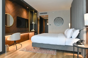 A modern hotel room with a large bed, a desk with a chair, a round mirror, a flat-screen TV, and a decorative wall piece. - Crowne Plaza Ankara by IHG (Ankara)