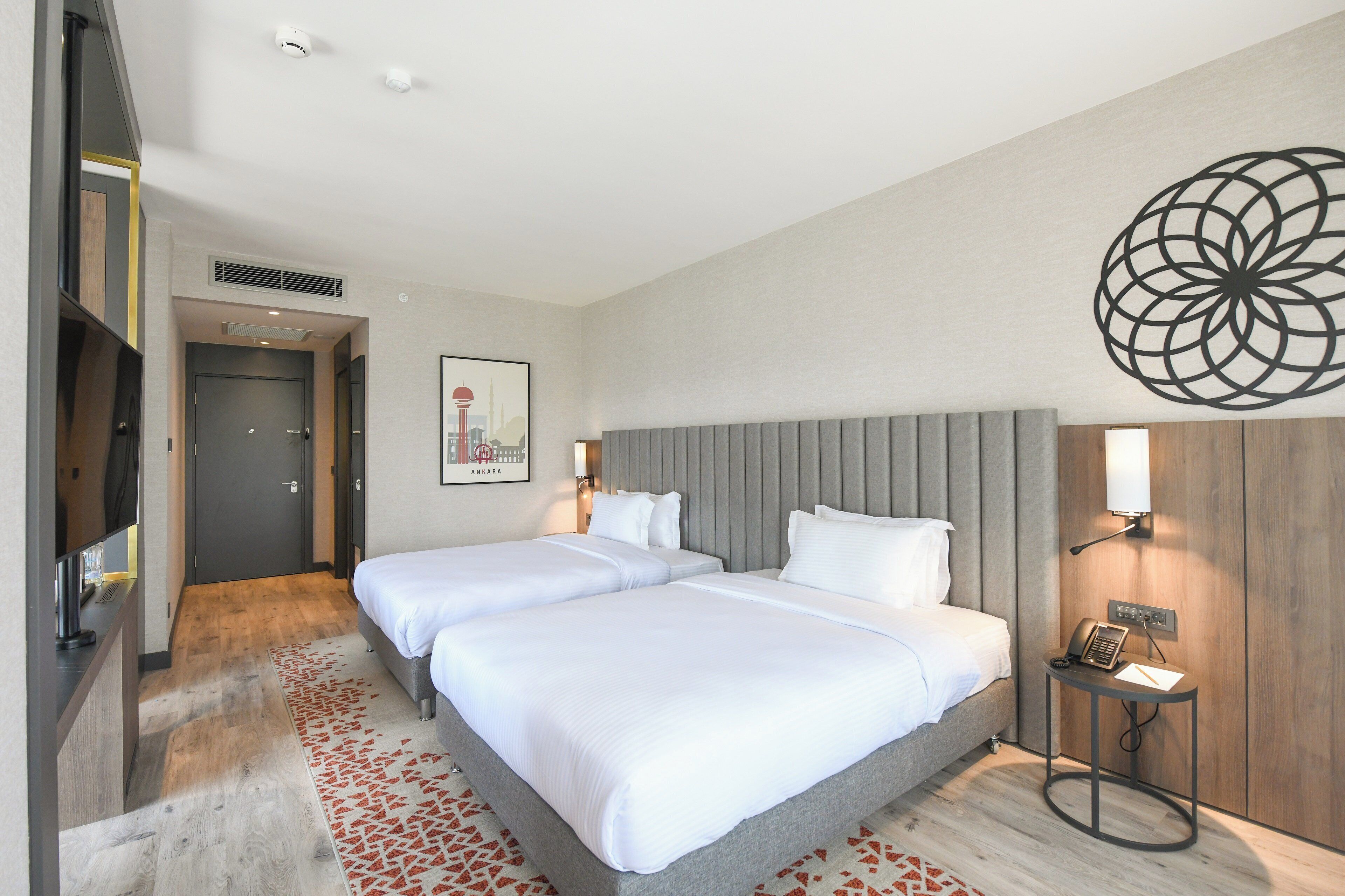 A hotel room with a double bed, a desk, a chair, a telephone, and a wall-mounted artwork.