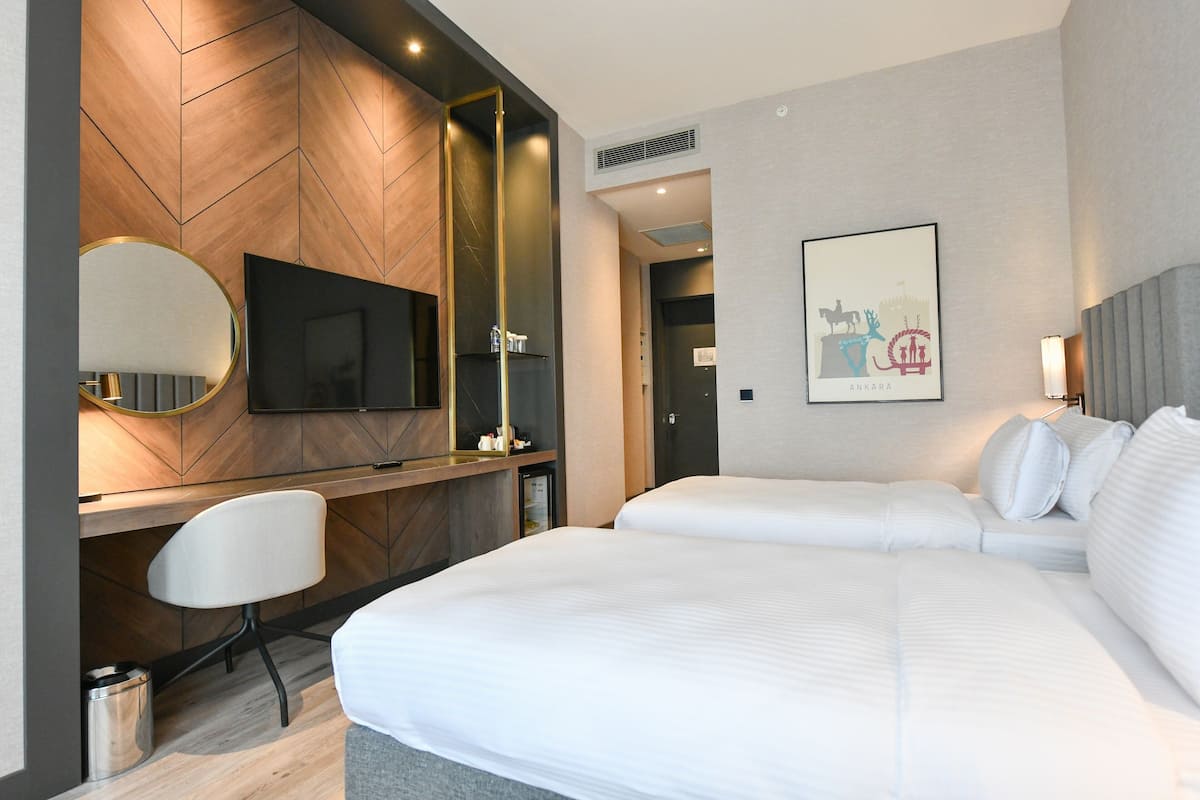 A modern hotel room with a large bed, a desk with a chair, a television, and a framed picture on the wall.