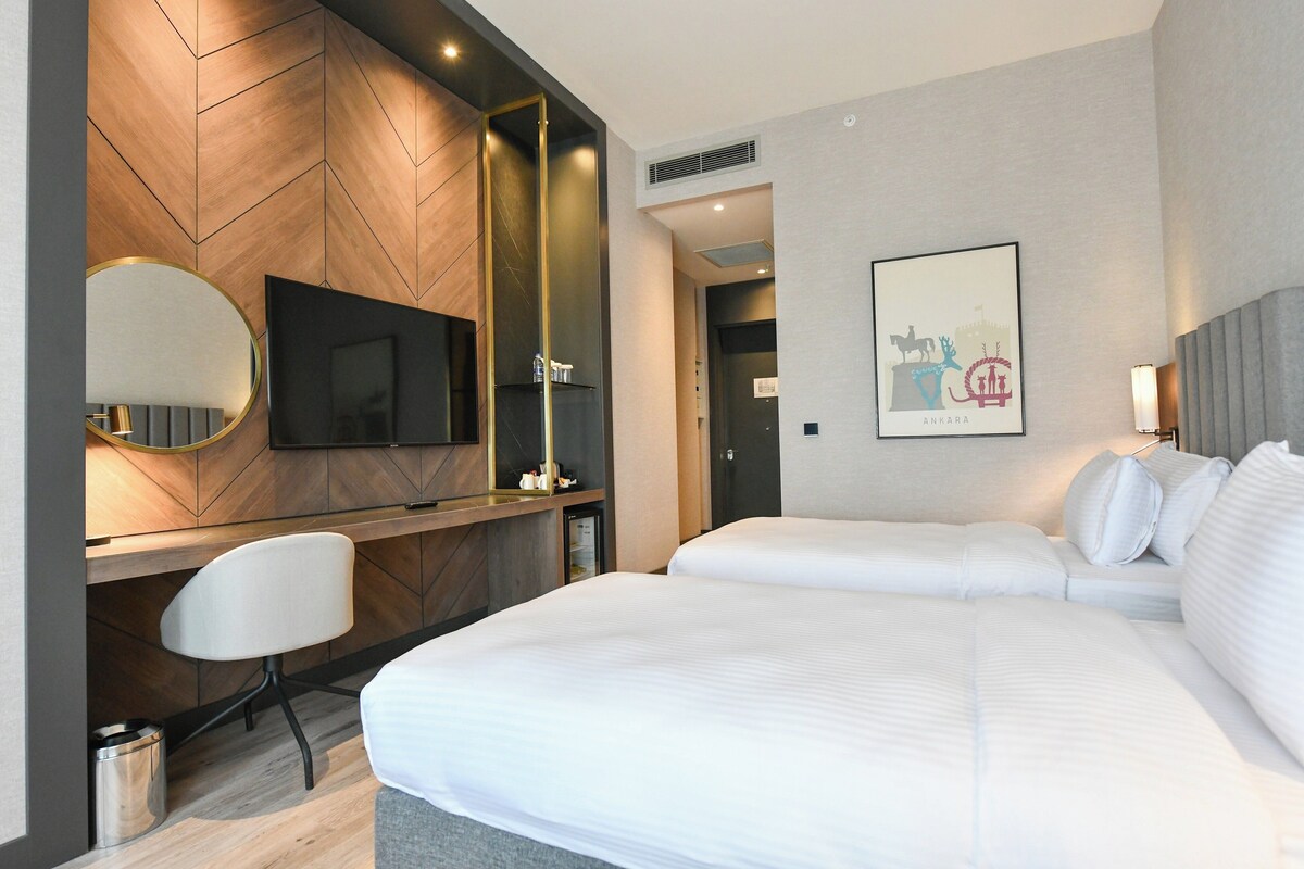 A modern hotel room with a large bed, a desk with a chair, a television, and a framed picture on the wall.