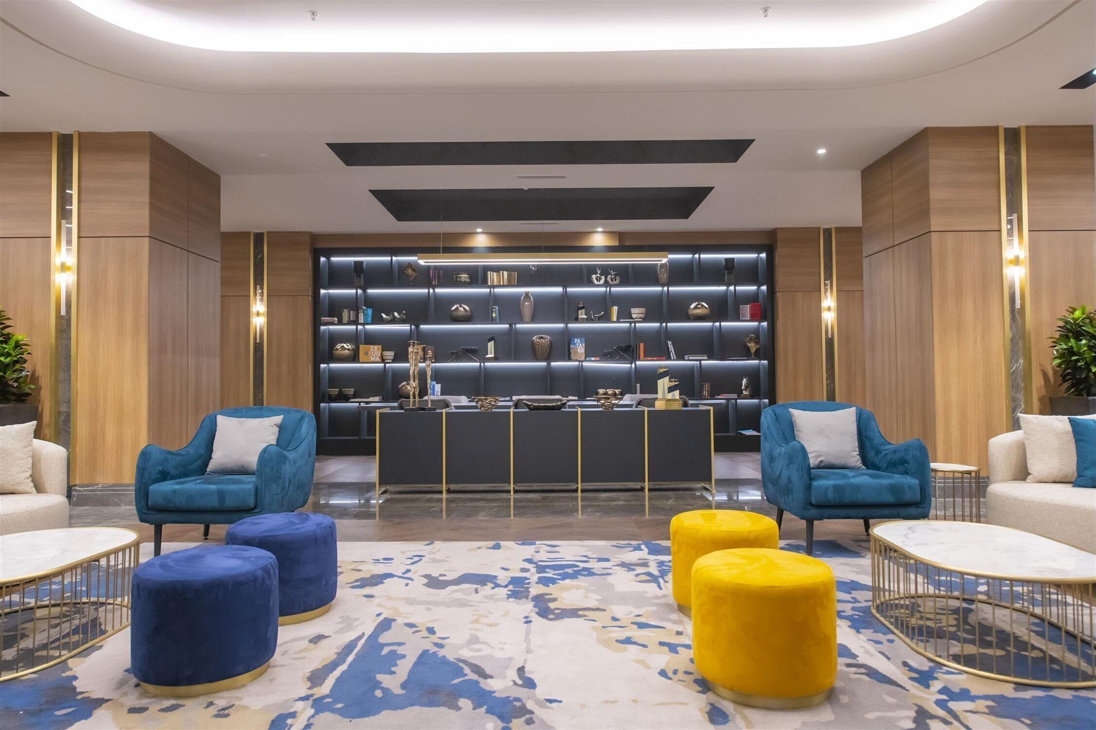 A modern lobby with blue and yellow ottomans, a reception desk, and a display of decorative items.