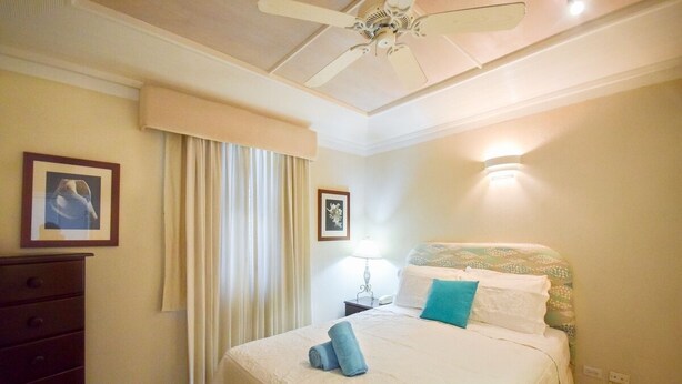 Une chambre à coucher comprenant un lit, une commode, un ventilateur de plafond et deux tableaux encadrés accrochés au mur.