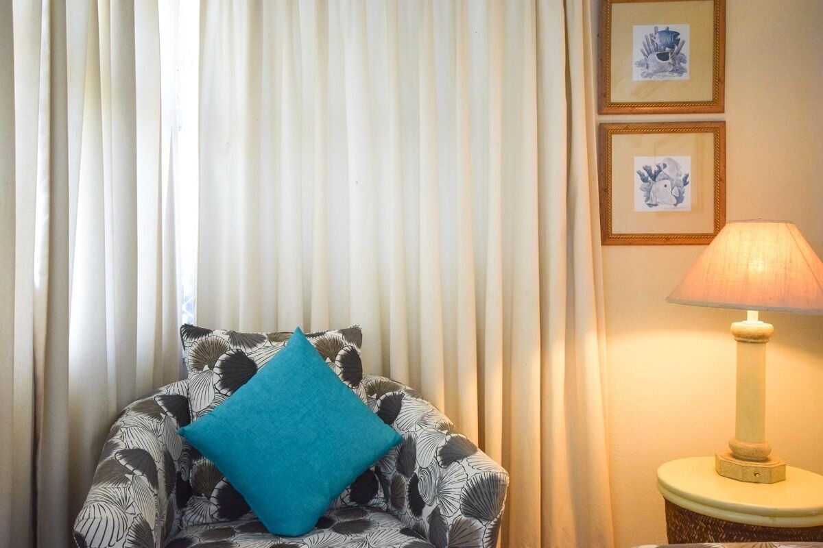 A room with a patterned armchair, a teal cushion, and a lamp on a side table.