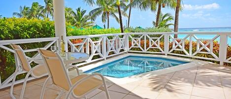 A pool area with a white fence, chairs, and a view of the ocean.