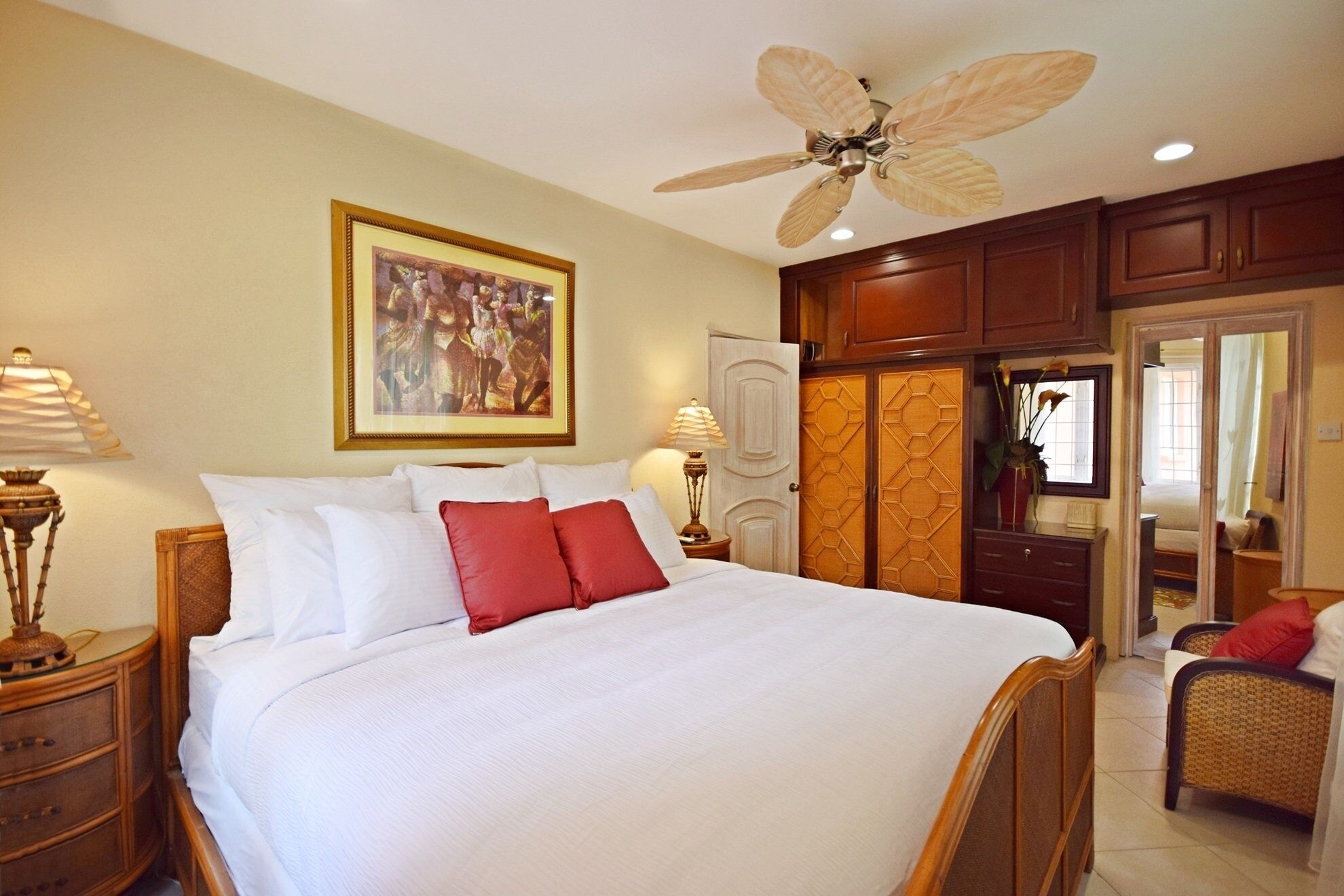A hotel room with a large bed, a ceiling fan, wooden cabinets, and a painting on the wall.
