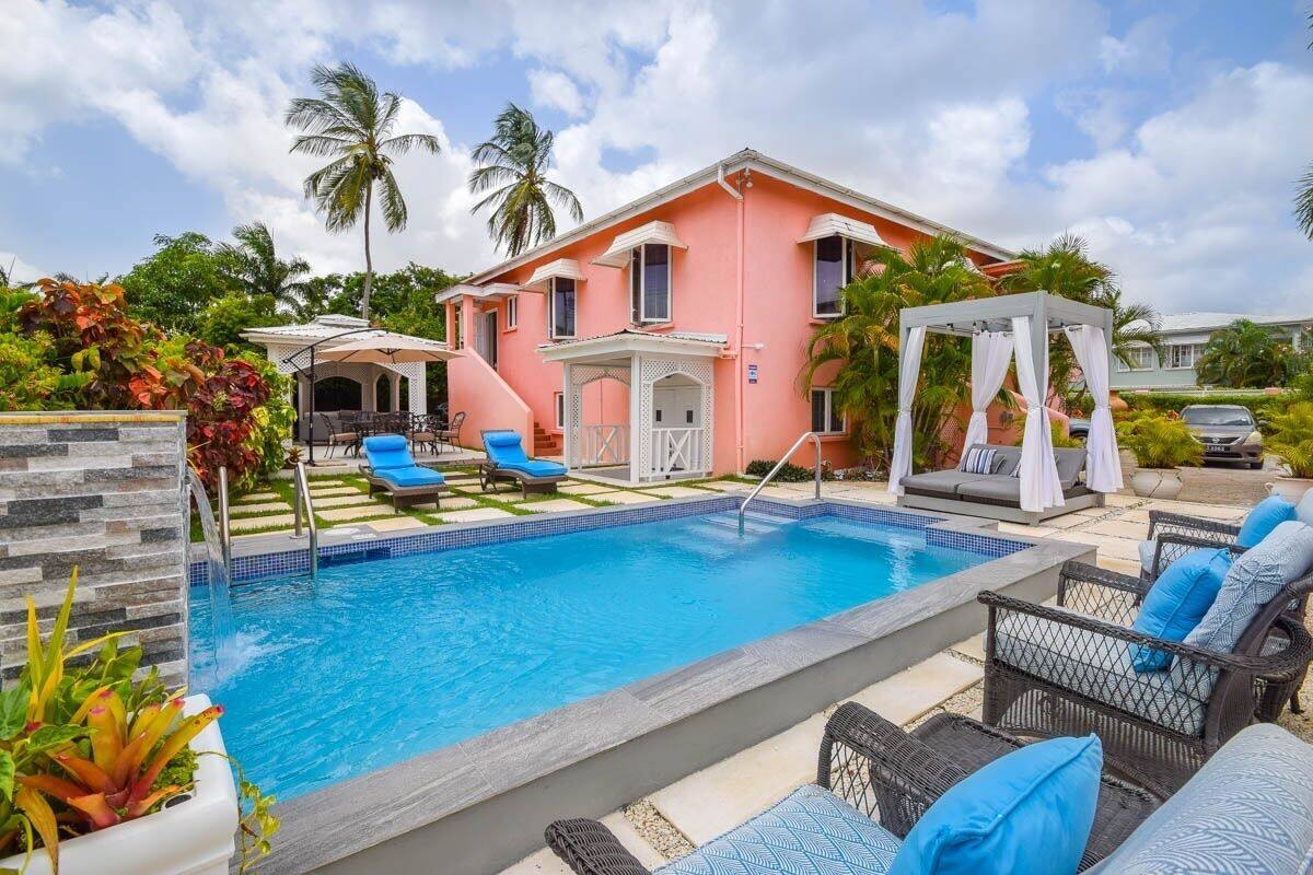 A pink building with a swimming pool, lounge chairs, and a gazebo.