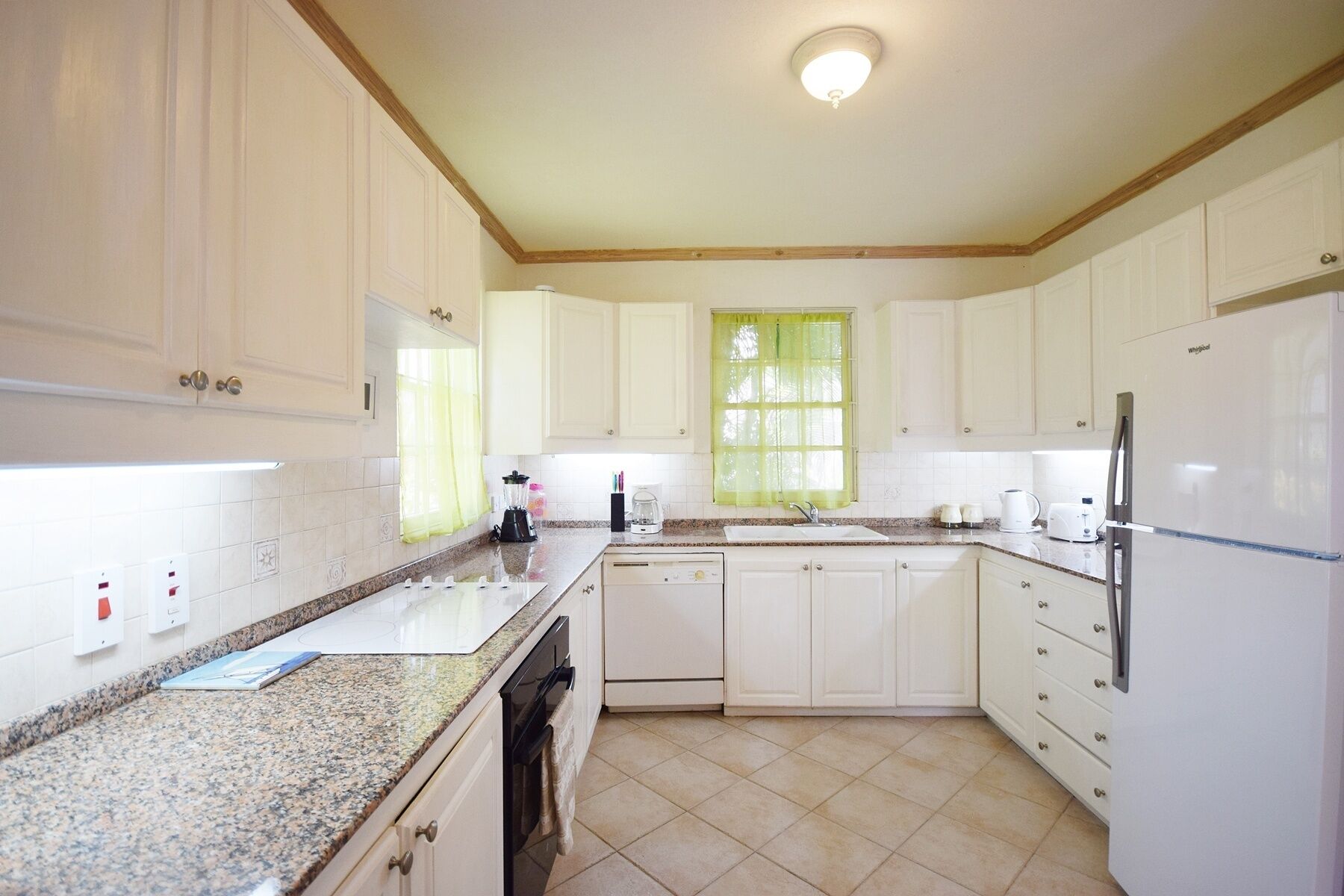 A kitchen with white cabinets, a granite countertop, a dishwasher, a refrigerator, and a window with a green curtain.