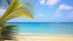 Een strand met helder turquoise water, een zandstrand en een zeilboot in de verte.