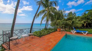 Zona junto a la piscina con vista al océano, palmeras y un suelo de baldosas.