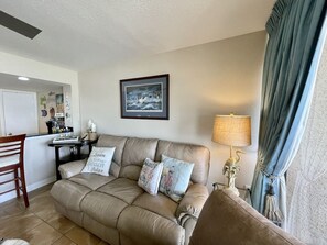 A living room with a beige leather sofa, a dining table with chairs, a lamp, and a framed picture on the wall.