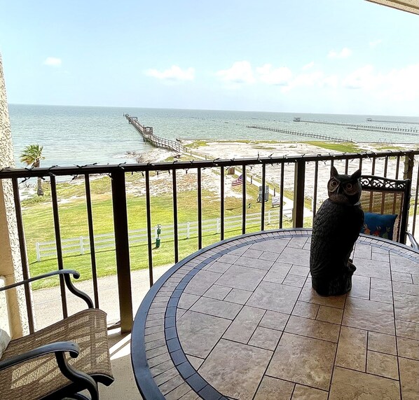 A balcony with a view of the ocean, a chair, and a decorative owl statue.