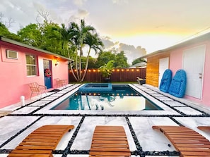 Una piscina con tumbonas de madera, un edificio rosa y una valla de madera.
