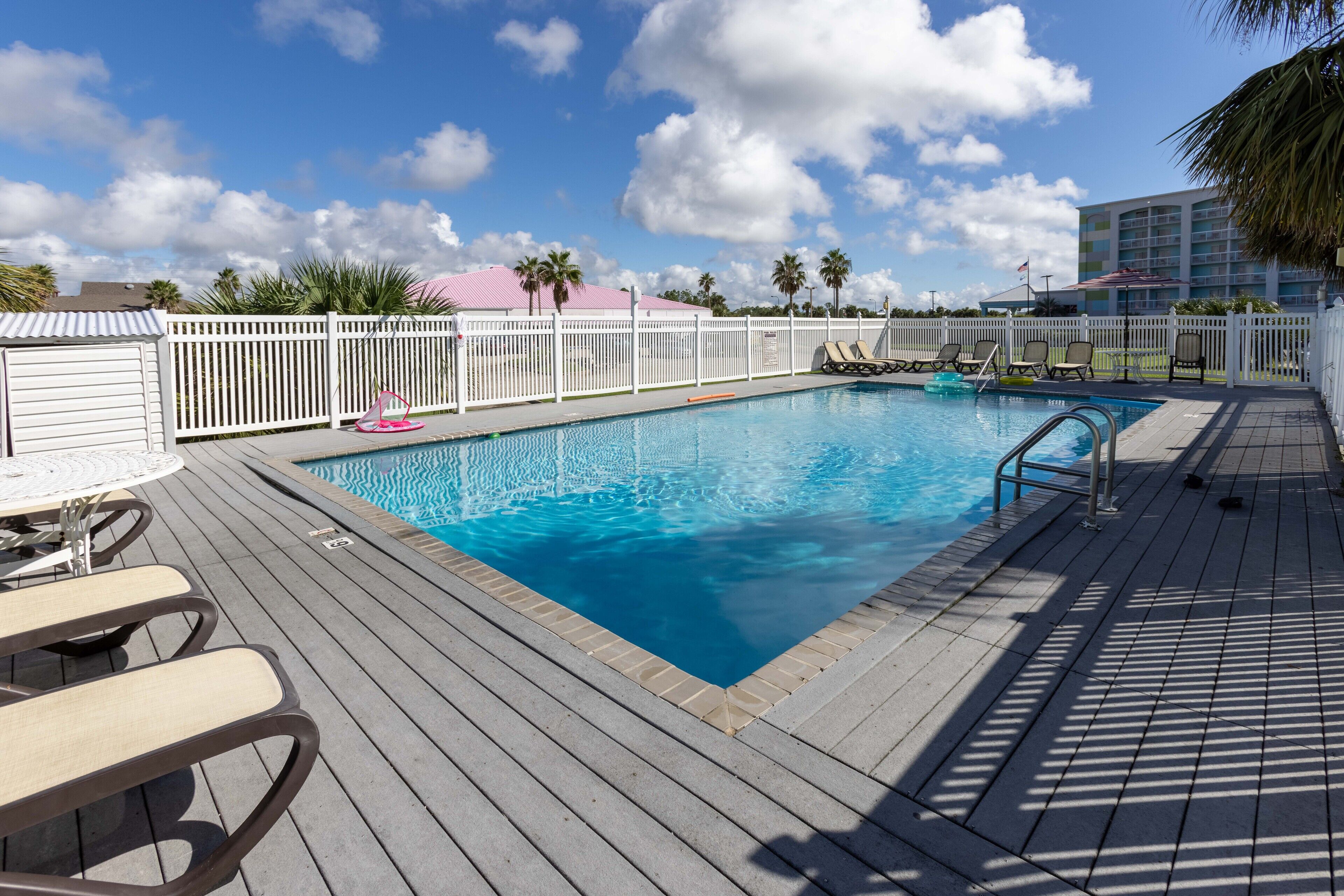 Une piscine avec une terrasse en bois, des chaises longues et une clôture blanche.