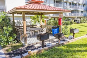 A covered outdoor seating area with a table and chairs, barbecue grills, and a trash bin. - "Sunshine At The Beach - Fall Specials! Many Upgrades! Perfect Location! (Orange Beach)
