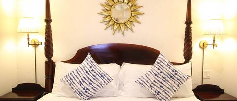 A neatly made bed with white and blue patterned pillows, a wooden headboard, and a sunburst mirror on the wall.