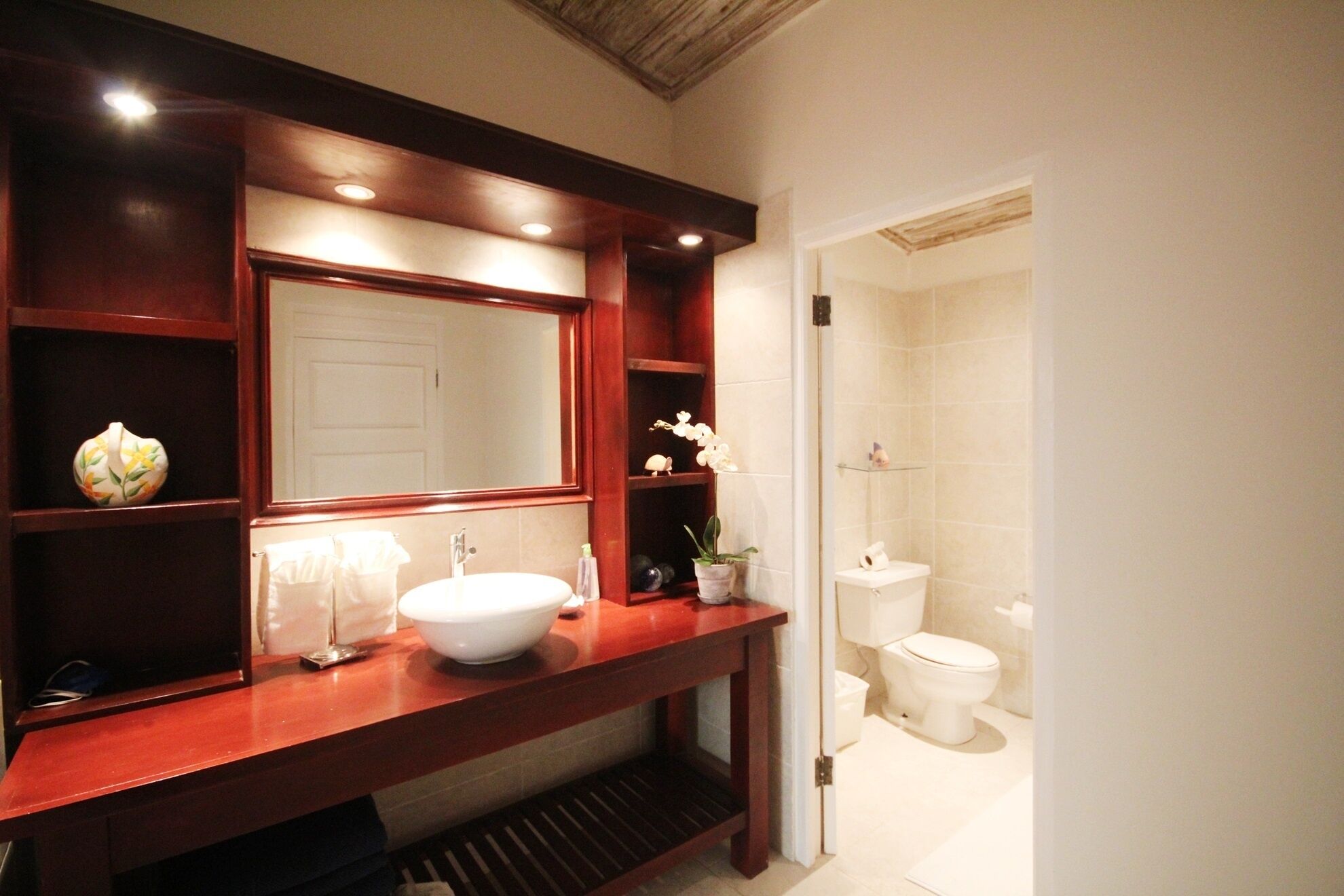 A bathroom with a wooden vanity, a large mirror, a white sink, and a toilet.