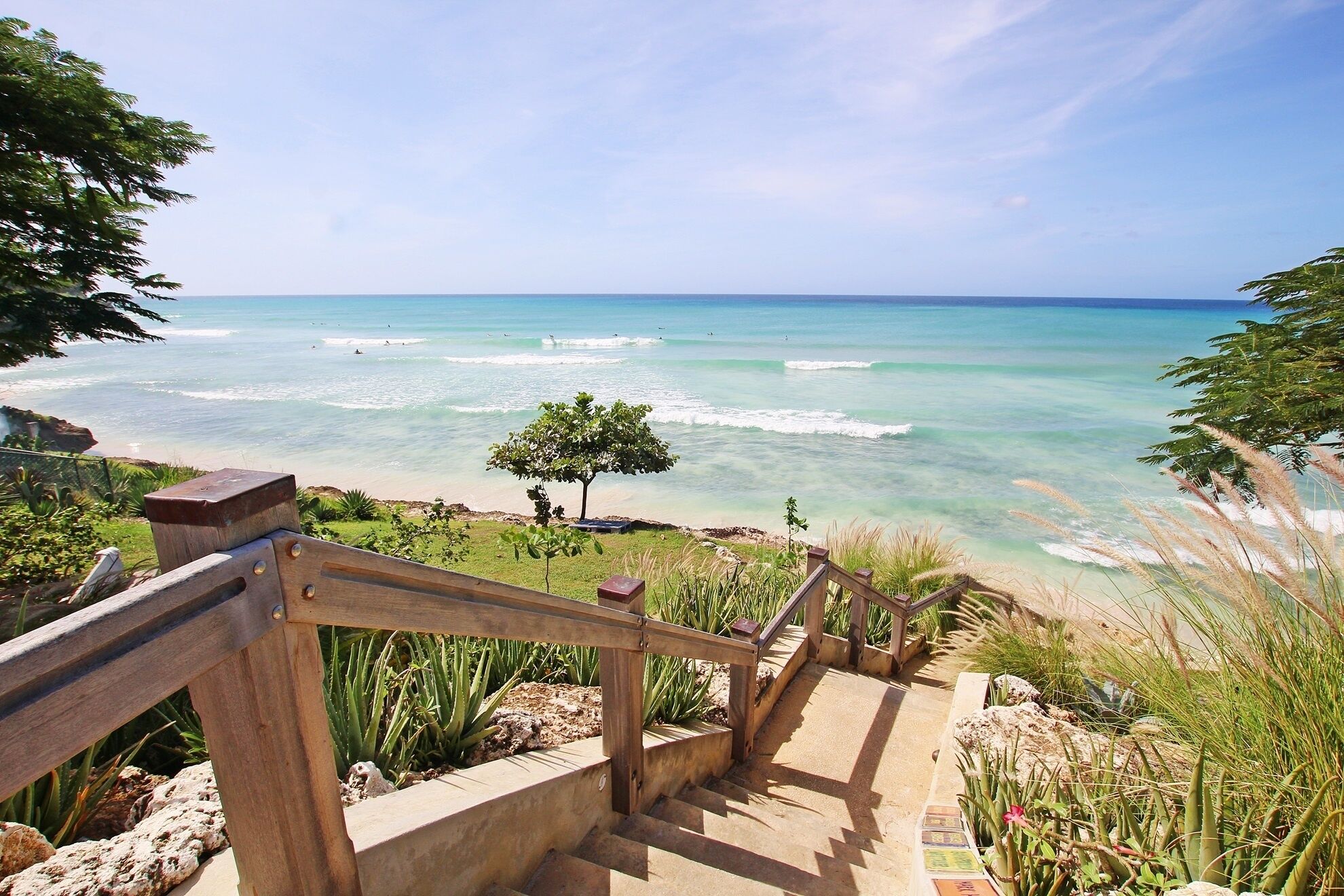A wooden staircase leading to a beach with clear turquoise water and waves.