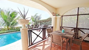 A poolside area with a table and chairs, a decorative plant, and a view of the pool and surrounding greenery. - Oceanfront 2-bed Apt With Pool Near Surfing - Rosalie #2 2 Bedroom Apts by Bluescape (Oistins)