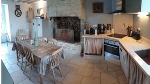 A kitchen with a stone fireplace, a dining table with chairs, a small island with a sink, and a stove. - Normandieheritage14 Cottage du Marais Omaha Beach D-Day Tour Guide E-bike Hiking (Canchy)