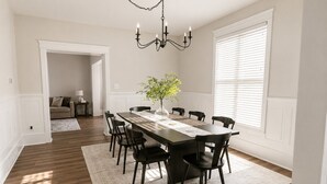 Une salle à manger avec une longue table, des chaises, un lustre et un vase rempli de fleurs.