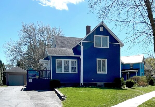 Une maison à deux étages avec un garage, une pelouse devant et un ciel bleu dégagé.