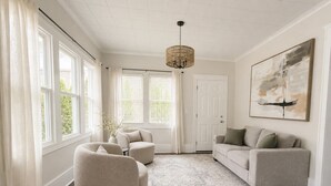 Un salon spacieux avec une grande fenêtre, un lustre, un canapé et un tapis.