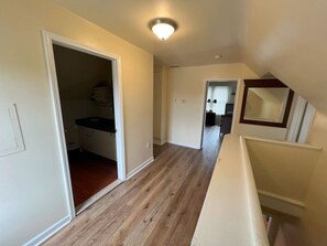 Un pasillo con piso de madera, un armario con encimera negra y una puerta que da a otra habitación.