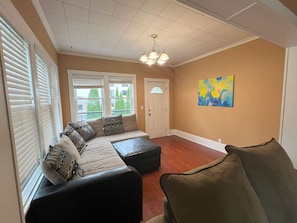 A living room with a sectional sofa, ottoman, and a painting on the wall. - Flint Haus - Frankenmuth Vacation Homes (Frankenmuth)