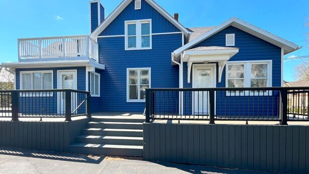 A two-story house with a balcony, a front porch, and a set of stairs leading to the entrance.
