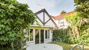 Een tuin met een wit huis, een ronde tafel en metalen stoelen.