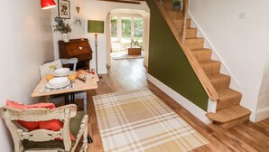 Een knus interieur met een houten trap, een eetruimte met een gedekte tafel, en een uitzicht op een tuin door een open deur.
