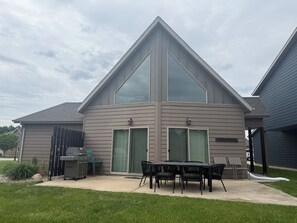 A modern two-story house with a patio, a grill, and a dining area.