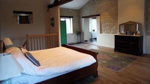 Een slaapkamer met een houten bed, een dressoir en een stenen muur.