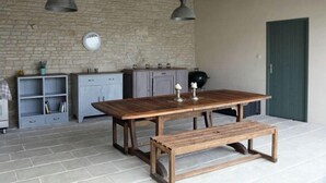Een rustieke keuken met een grote houten tafel, twee hangende吊灯 en een stenen muur.