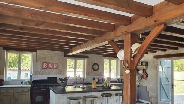 Een landelijke keuken met een stenen muur, houten balken, een barbord en een groot eiland met krukken.