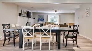 A dining area with a long table, white and dark chairs, a fireplace, and artwork on the walls. - Large home & 5 min to Kalahari, Gather here at WOODLAND RETREAT! (Pocono Summit)